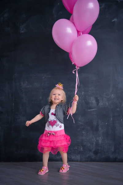 themed birthday for a fun emotional girl of the blonde smash the cake in pink color on a black background. stylized photo session tradition with sweet decor and balloons