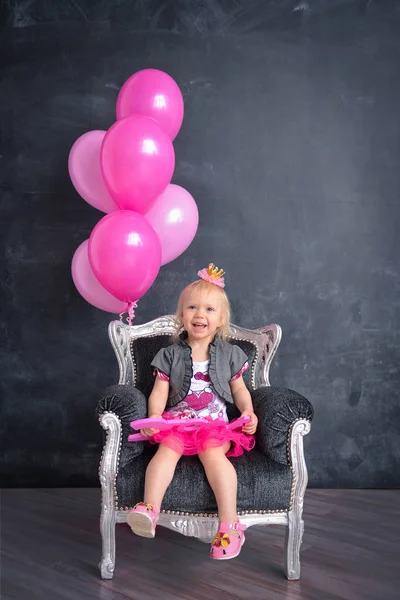 Compleanno a tema per una divertente ragazza emotiva della bionda spacca la torta in colore rosa su uno sfondo nero. tradizione sessione fotografica stilizzata con decorazioni dolci e palloncini — Foto Stock