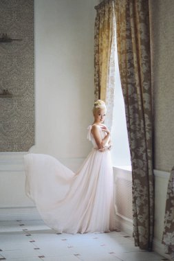 Gelinin resimdeki sarışın kız bir uçan parlak elbise penceresinde yakın duruyor. Düğün fotoğraf. nazik sakin görüntü. Küçük gürültü