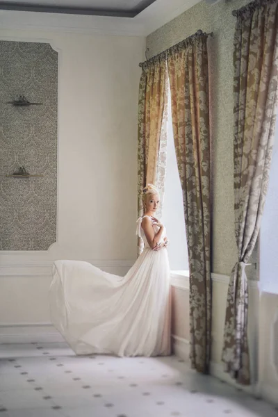Chica rubia en la imagen de la novia se encuentra cerca de la ventana en un vestido brillante volador. foto de boda. imagen tranquila suave. Ruido pequeño — Foto de Stock