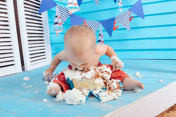 decoration for the boys birthday, smash the cake in a nautical marine style. stylized birthday ship photo shoot. Cheerful boy eats and break a cake with his hands on the first holiday
