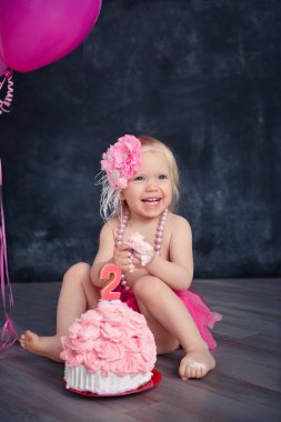 temalı doğum günü için eğlenceli bir duygusal kız sarışın siyah bir zemin üzerine pembe renkli pasta şut. stilize Fotoğraf oturumu geleneği ile tatlı dekor ve balon