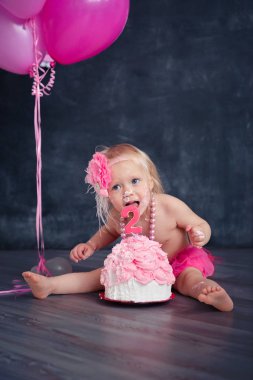 temalı doğum günü için eğlenceli bir duygusal kız sarışın siyah bir zemin üzerine pembe renkli pasta şut. stilize Fotoğraf oturumu geleneği ile tatlı dekor ve balon