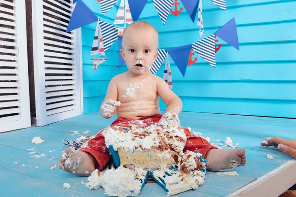 decoration for the boys birthday, smash the cake in a nautical marine style. stylized birthday ship photo shoot. Cheerful boy eats and break a cake with his hands on the first holiday