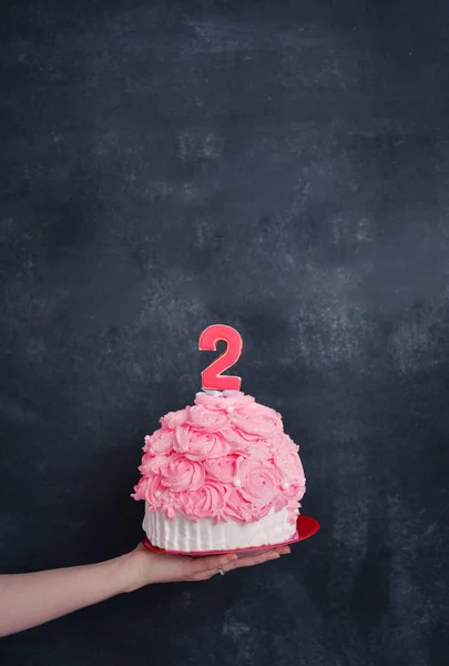 Тематичний день народження для веселої емоційної дівчини блондинки розбиває торт рожевим кольором на чорному тлі. стилізована традиція фотосесії з солодким декором і повітряними кулями — стокове фото
