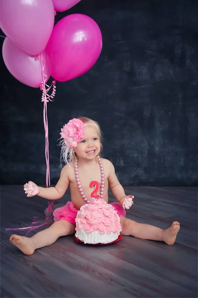 themed birthday for a fun emotional girl of the blonde smash the cake in pink color on a black background. stylized photo session tradition with sweet decor and balloons