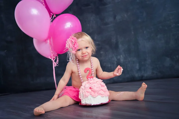 themed birthday for a fun emotional girl of the blonde smash the cake in pink color on a black background. stylized photo session tradition with sweet decor and balloons