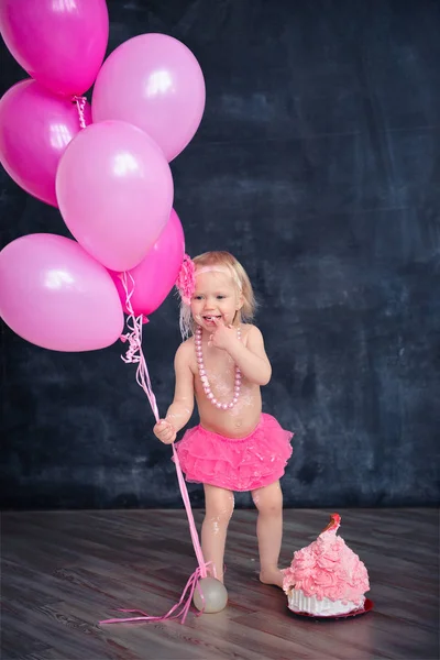 themed birthday for a fun emotional girl of the blonde smash the cake in pink color on a black background. stylized photo session tradition with sweet decor and balloons