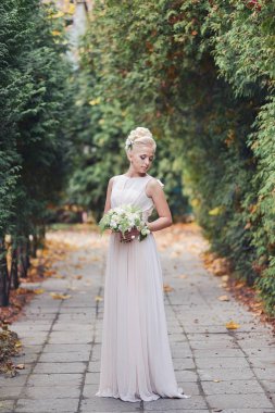 güzel zarif sarışın gelin alışılmadık bir sonbahar buket ile yolda bir parkta duruyor