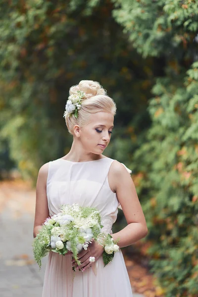 Красивая элегантная блондинка невеста стоит в парке на дороге с необычным осенним букетом — стоковое фото