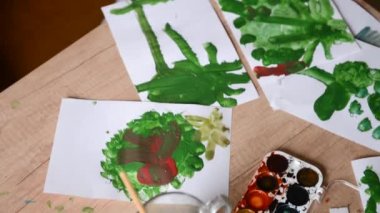 Genç sanatçının yeşil dönemi eserlerinde. Çocuk çizimleri suluboya boyalar, fırçalar arasında masadaki. Çocuk Sanat