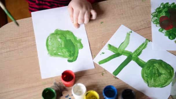 Kinderhände malen Aquarelle auf die Oberfläche eines Holztisches auf Papier. Kinder Kreativität, Familie Hobby Aquarellmalerei Gemälde — Stockvideo