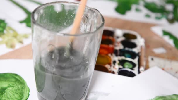 Veverka štětec máchání ve sklenici špinavé vody z akvarelů. tvůrčí nepořádek na stole zblízka tvůrčí proces — Stock video