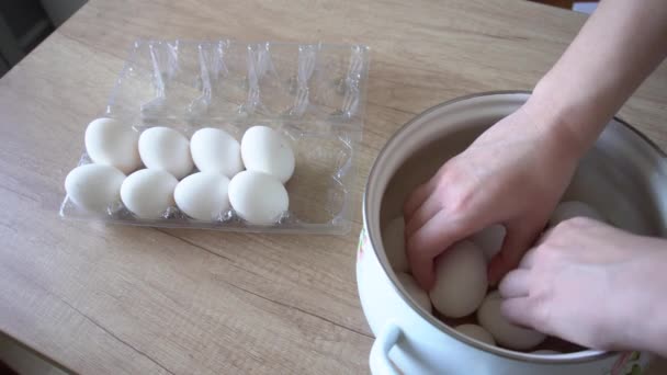 Les mains féminines déplacent les œufs de poulet d'une boîte en plastique dans une grande casserole blanche sur une table en bois — Video