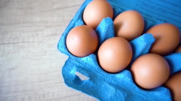 Натуральные органические куриные яйца птицы в эко-картонной бумаге, завернутой в синий цвет на деревянном столе крупным планом — стоковое видео