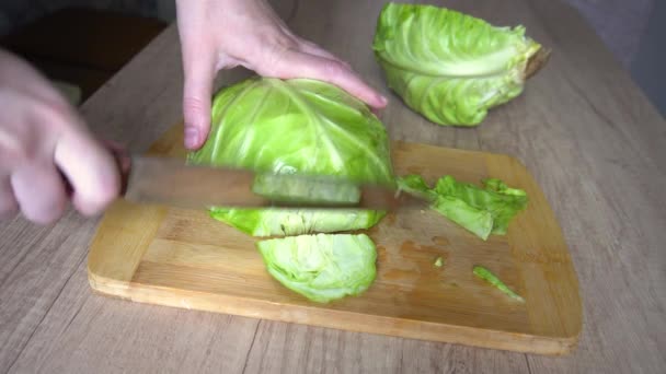 As mãos femininas cortam o repolho verde em uma superfície de madeira da mesa de cozinha — Vídeo de Stock