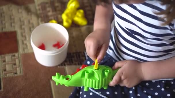 El niño juega en el interior en un sofá con el kit de construcción de diseño en forma de dinosaurio. Los dedos de los niños recogen un juguete rompecabezas de color brillante con un destornillador . — Vídeos de Stock