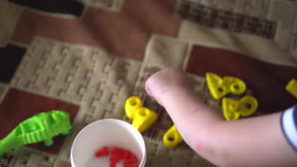 Chica examina los detalles del rompecabezas de diseño de niños. Patas de dinosaurio amarillo acostado en el sofá y los pernos están en la caja . — Vídeos de Stock