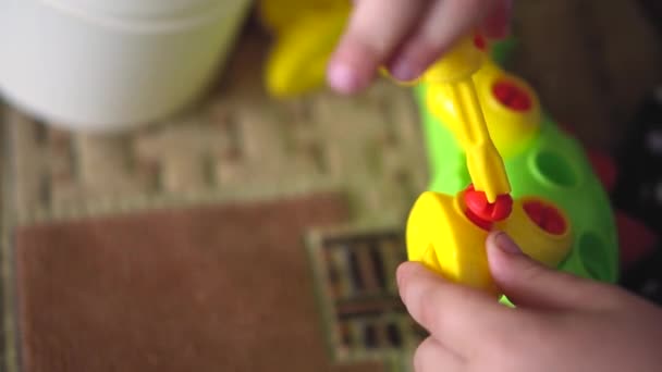 Het kind speelt binnenshuis op een bank met de Designer bouwpakket in de vorm van een dinosaurus. Childrens vingers verzamelen een helder gekleurde puzzel speelgoed met een schroevendraaier. Close-up — Stockvideo