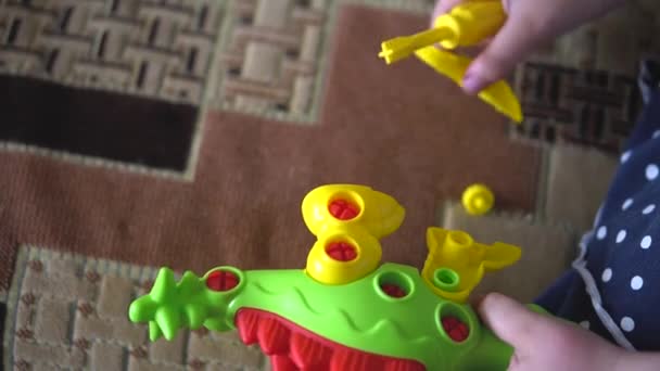 Ragazza del bambino che gioca al chiuso sul divano con un kit di costruzione di design sotto forma di dinosauro. Le dita dei bambini raccolgono un puzzle multicolore brillante con un cacciavite per piedi di dinosauro — Video Stock