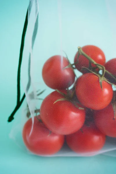 Dojrzała gałąź pomidorów wiśniowych leży w torebce wielokrotnego użytku na białym tle niebieskim. do czynienia z jednorazowymi plastikowymi torbami Obraz Stockowy