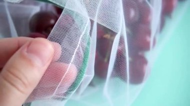 kadın el plastik le mücadelede mavi arka plan üzerinde yeniden kullanılabilir kumaş şeffaf çanta kiraz dokunur