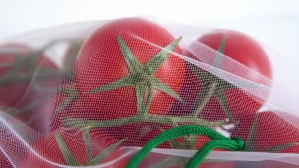 Una rama madura de tomate cherry se encuentra en una bolsa de reutilización reutilizable sobre un fondo blanco aislado. para tratar con bolsas de plástico desechables — Vídeos de Stock