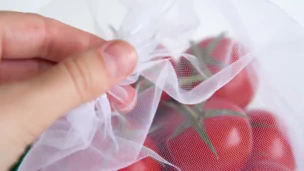 Mano femenina toca rama madura de tomate cherry se encuentra en bolsa de reutilización reutilizable sobre un fondo blanco aislado. para tratar con bolsas de plástico desechables — Vídeos de Stock