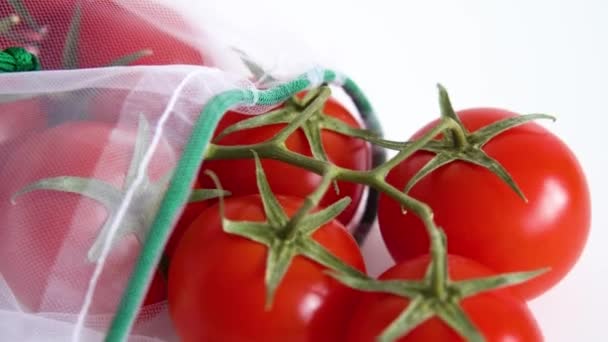 Una rama madura de tomate cherry se encuentra en una bolsa de reutilización reutilizable sobre un fondo blanco aislado. para tratar con bolsas de plástico desechables — Vídeos de Stock