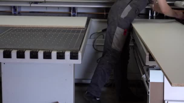 Hombre trabajador recibe una pieza de aglomerado laminado en un centro de formato raskroyechny con control de programa numérico en la fábrica de fabricación de muebles — Vídeos de Stock