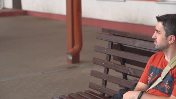 Unatkozó ember ül padon kívül, és úgy néz ki, az óra ideges — Stock videók