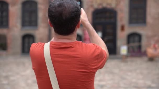 Šťastný usměvavý turecký turista si po telefonu na turné po Bělorusku na hradě Mir vezme fotografie a videozáznamy. — Stock video