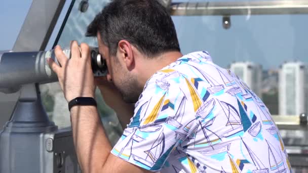 El turista masculino mirando el paisaje urbano a través de prismáticos en la plataforma turística — Vídeos de Stock
