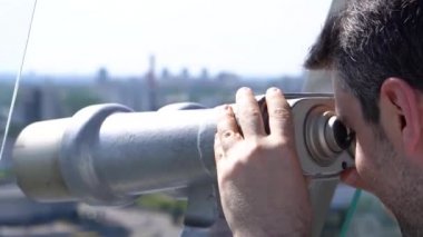 Gezi platformunda dürbünle şehir manzarasına bakan erkek turist
