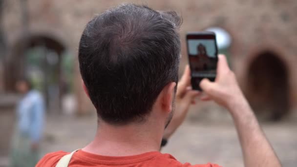 Heureux touriste souriant prend des photos et des vidéos sur son téléphone lors d'une tournée en Biélorussie dans le château de Mir. gros plan, vue arrière — Video