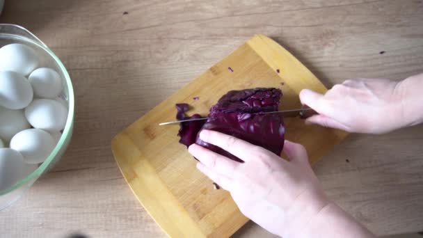 Les mains féminines coupent avec le couteau le chou rouge sur la table en bois. Préparer un colorant naturel pour les œufs de Pâques bleus — Video