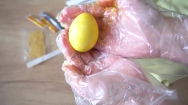 Mutlu Paskalya tatiline hazırlanıyorum. Şeffaf koruyucu eldivenler içindeki ustanın elleri yumurtayı sarı altın rengine boyamanın sonucunu gösterir. Ahşap arkaplanda üst görünümü kapat.