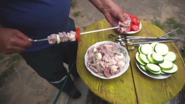 Kebabs koken. Mannelijke hand snaren stukken vlees op spiesje op een zomerdag buiten. gemarineerde vlees en tomaten doorboord op een houten achtergrond een rustieke levensstijl — Stockvideo