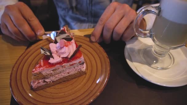 Fechar a mão de um homem, quebrá-lo e comer pedaço de bolo com um garfo em uma mesa em um café dentro de casa — Vídeo de Stock