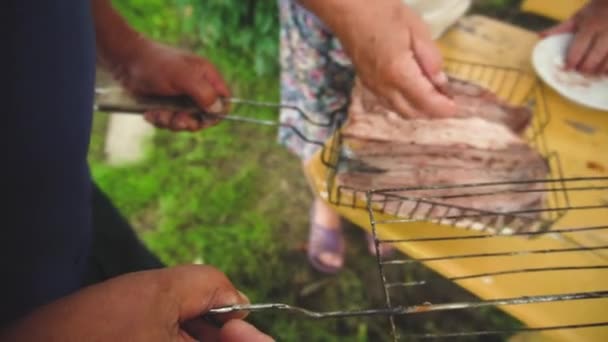 Par de manos de hombres y mujeres prisioneros poniendo carne al pescado para asar de cerca - Concepto de cocinar barbacoa y compartir una comida al aire libre. Estilo de vida — Vídeo de stock