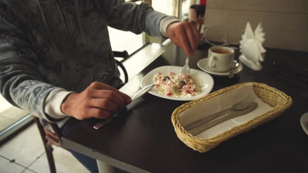 Imagen recortada del hombre durante una pausa para el almuerzo que come una ensalada fresca y saludable mientras está sentado en una mesa de madera — Vídeos de Stock