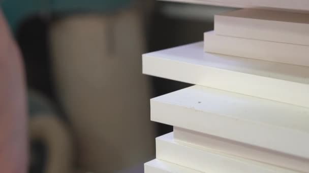 Stapel houten onderdelen op de voorgrond close-up, op de achtergrond een wazige mannelijke handen slijpen een houten detail in een meubelproductie — Stockvideo