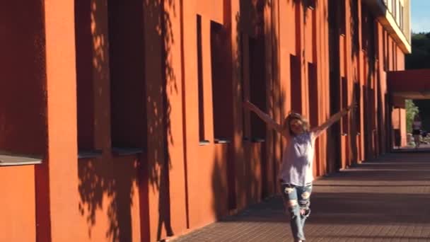 행복한 젊은 여자 금발은 도시 배경의 붉은 벽의 배경에 간다. 캐주얼 한 옷에 찢어진 청바지와 셔츠 — 비디오