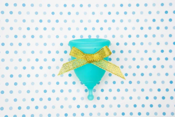 Copa menstrual azul con lazo de oro como regalo sobre un fondo blanco con lunares azules. higiene femenina durante el período, vista superior —  Fotos de Stock
