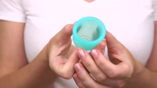 Руки молодой женщины демонстрируют крупным планом синюю менструальную чашку, средство личной гигиены во время менструации — стоковое видео