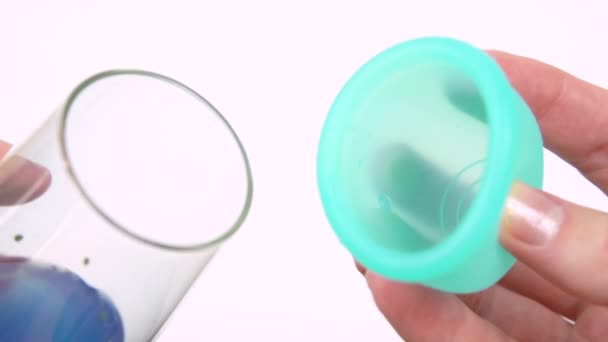 Händerna på en ung kvinna demonstrera arbetet i menstruations cupen med ett genomskinligt glas och blå vätska. intim hygienprodukt under period tid närbild — Stockvideo