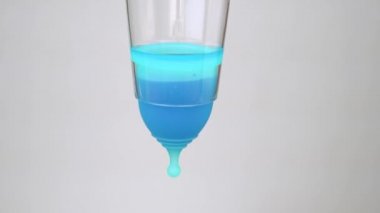 genç bir kadının elleri şeffaf bir cam ve mavi sıvı ile adet fincan çalışmalarını göstermektedir. dönem boyunca samimi hijyen ürünü