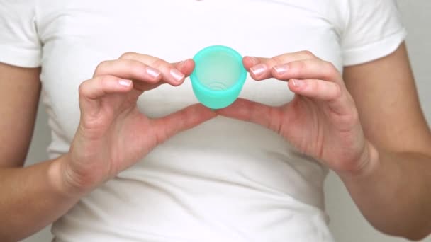 Händerna på ung kvinna visar närbild blå menstruations cupen, en personlig hygienprodukt under menstruation — Stockvideo