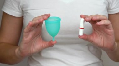 kadın karşılaştırmak ve adet yakın çekim sırasında kişisel hijyen ürünleri seçmek için elinde tampon lar ve mavi bir adet fincan tutar