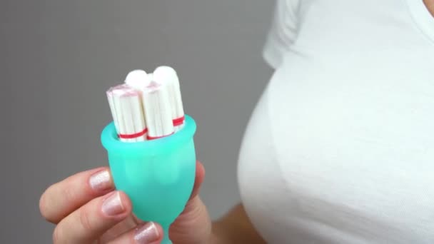 Mujer sostiene tampones y una copa menstrual azul en sus manos para comparar y elegir productos de higiene personal durante la menstruación de cerca — Vídeos de Stock